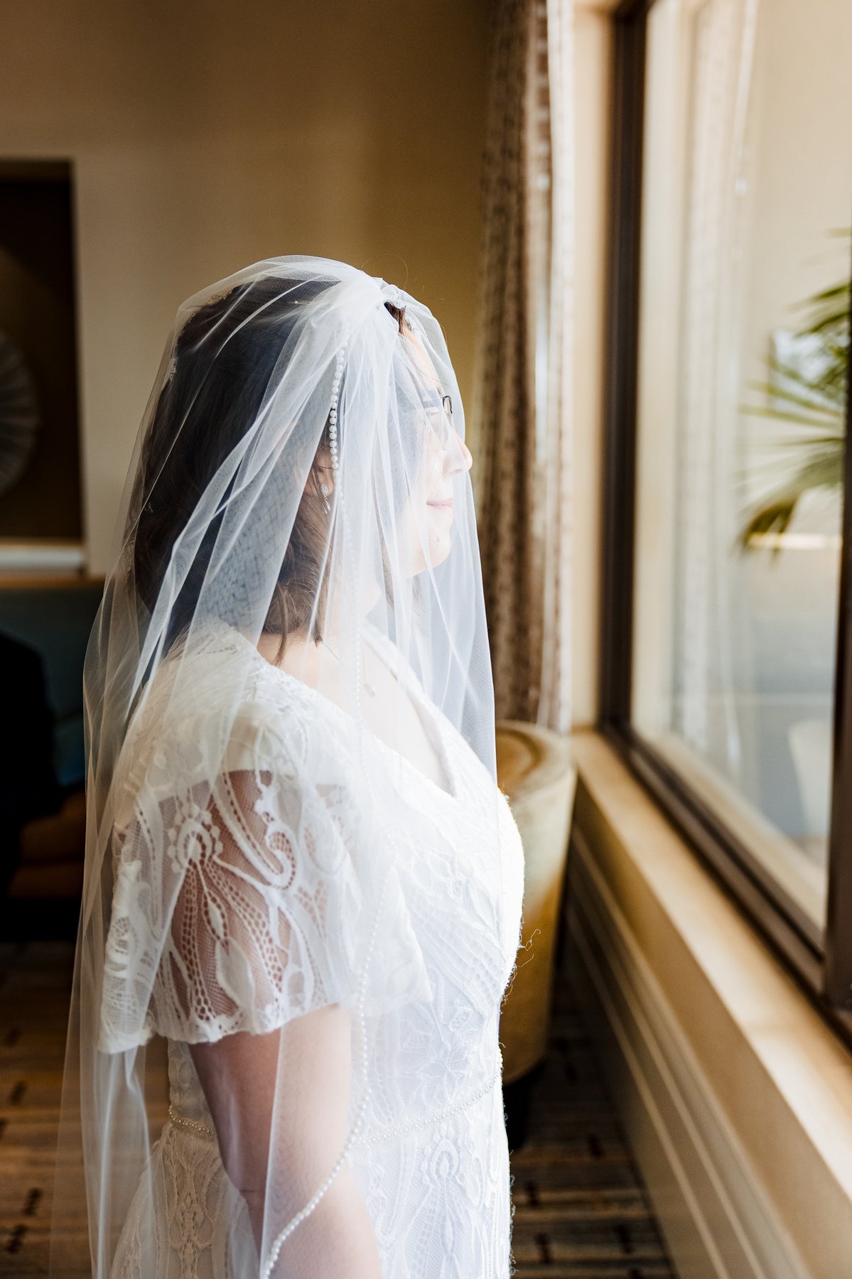 Bride in her veil and lace gown, profile portrait by the window before the Catholic wedding