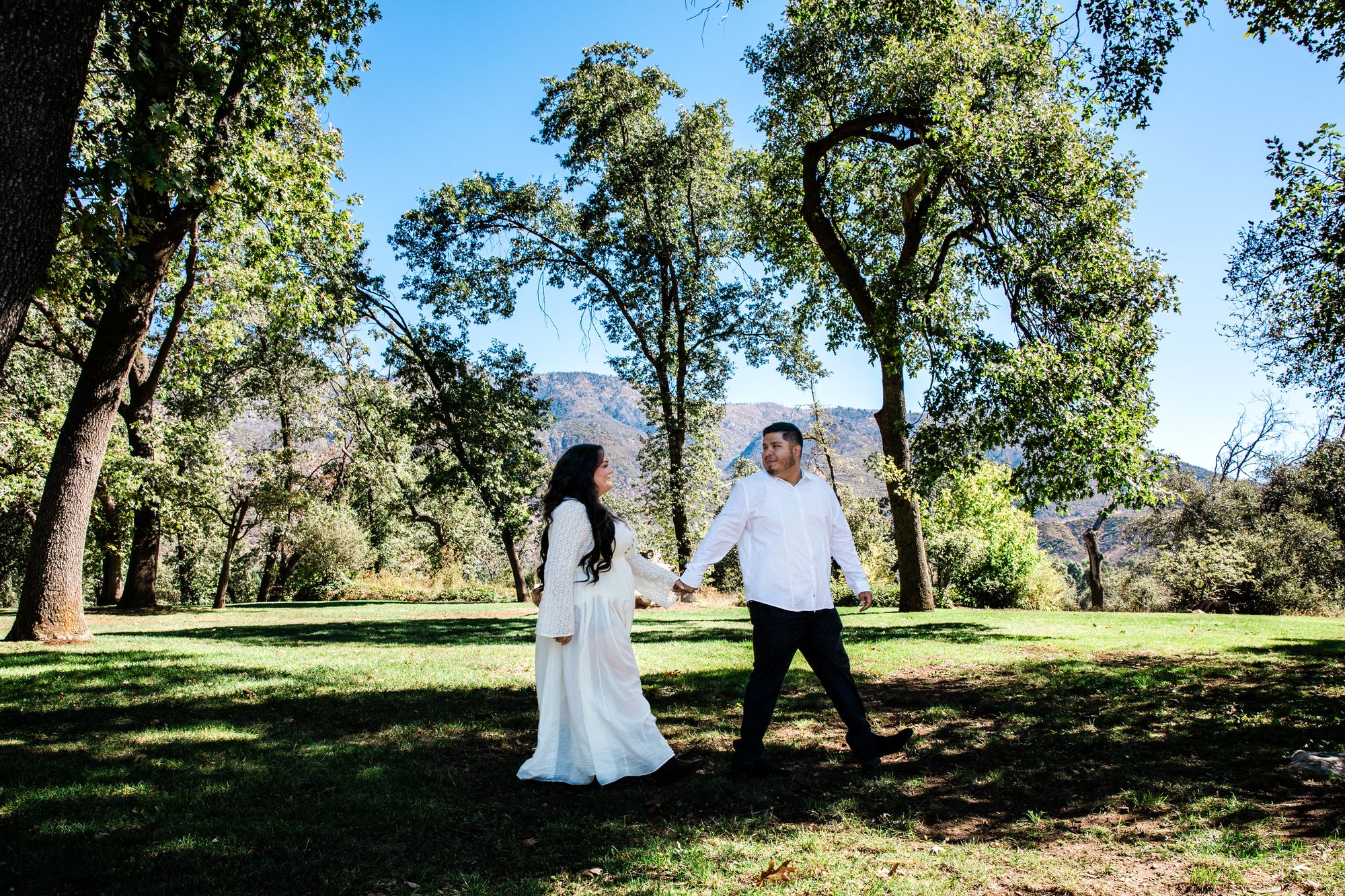 Eric and Cristina walking across a sunlit meadow at Oak Glen Preserve