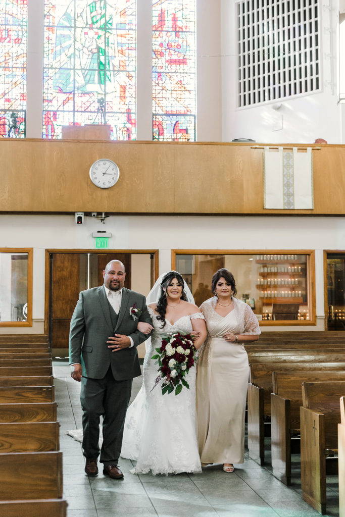 Bride walking down the isle with her parents at Holy Family Parish in Bellflower, California