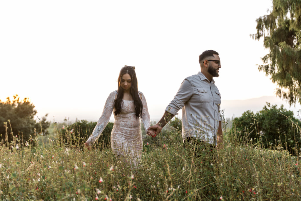 couple holding hands walking thru flowers at Prospect Park Redlands