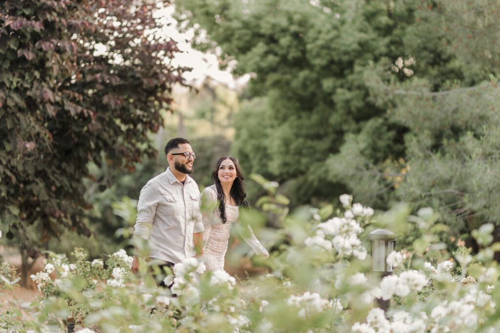 Couple walking thru flowers in Redlands at Prospect park during engagement session