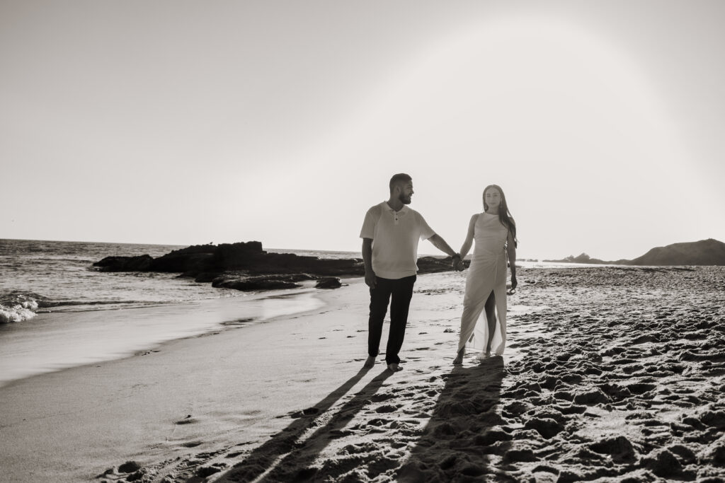 Black and white photo of couple walking on the laguna beach shore during sunset