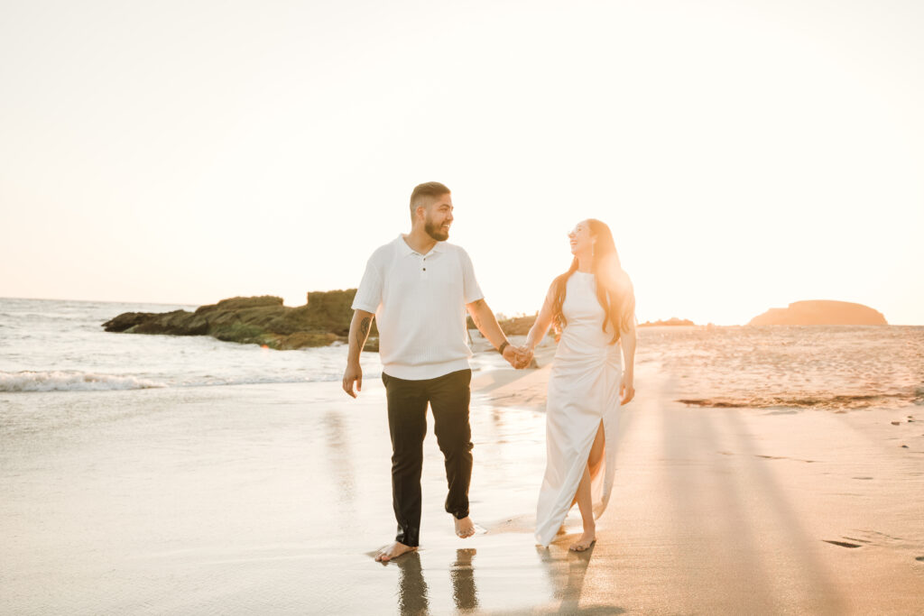 Couple Laughing while walking on laguna beach shore during engagement session
