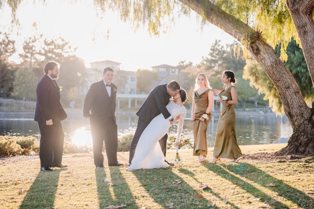Wedding party cheering as couple kisses outdoors at sunset near Murrieta lake venue