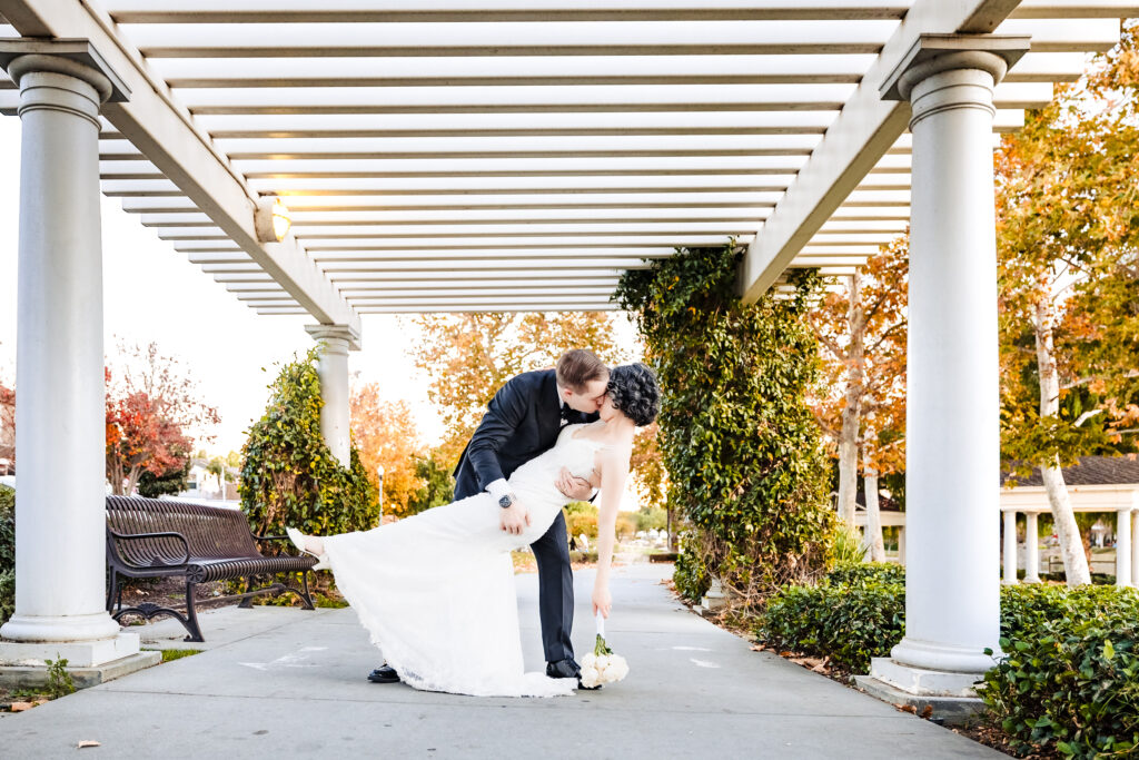 Bride and groom kiss under white pergola at outdoor reception space in Murrieta