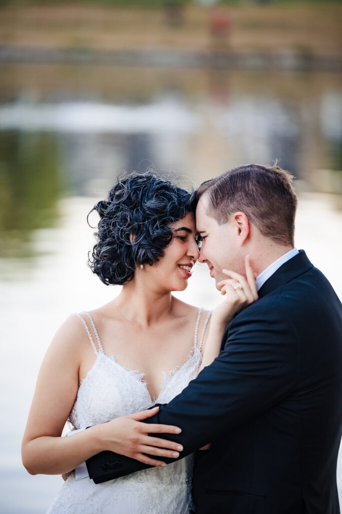 Bride and groom embrace beside lake at sunset during Murrieta Catholic wedding portrait session