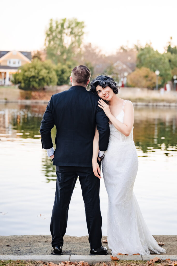 Bride rests her head on groom’s shoulder facing lake after ceremony at Saint Martha’s, Murrieta