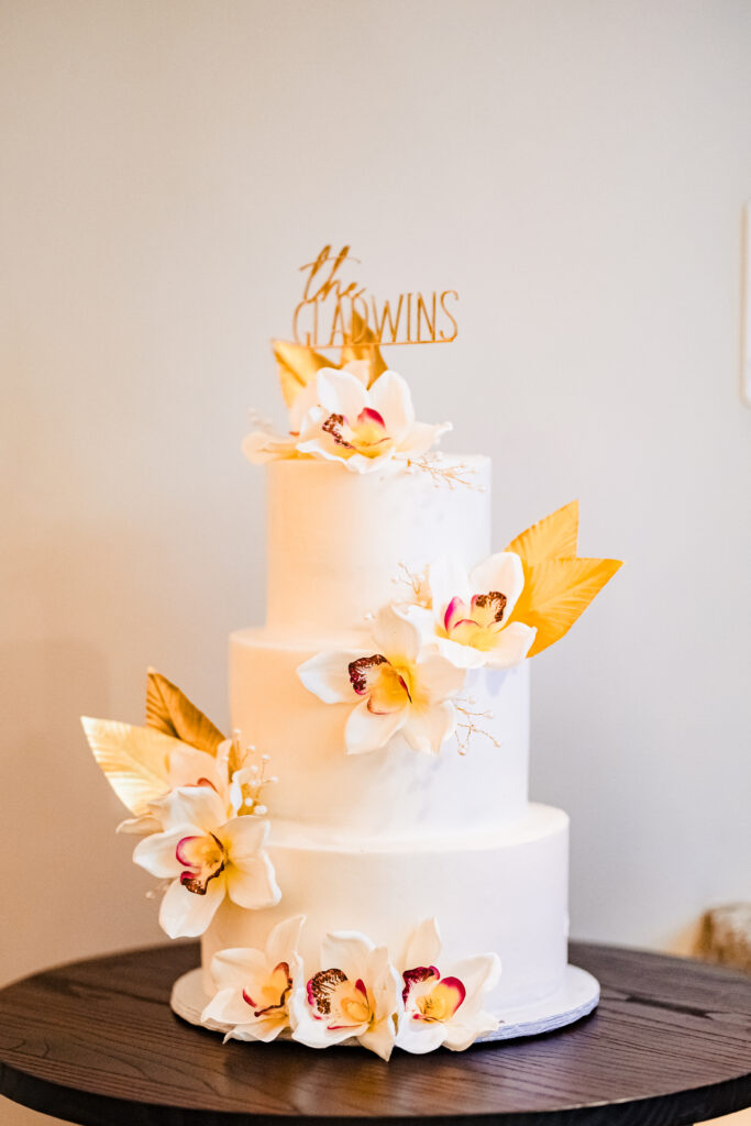 Modern white wedding cake with gold accents and orchid florals at reception in Murrieta