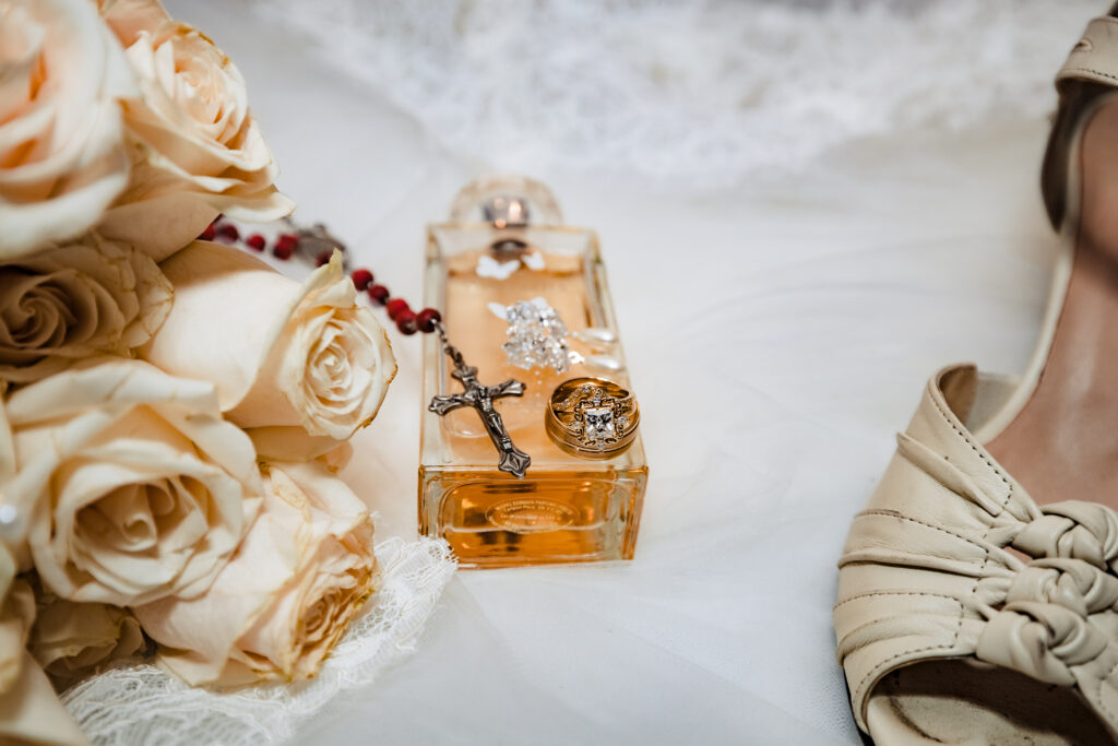 Flat lay of bridal bouquet, rosary, and perfume with soft ivory tones and lace veil