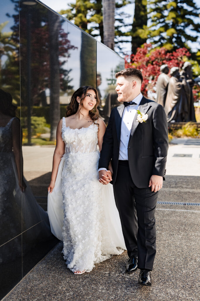 Candid bride and groom walking hand in hand through the sculpture gardens at Christ Cathedral in Garden Grove.